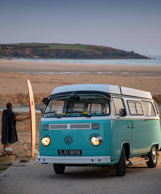 Surfing and a vintage VW campervan on a beach in Cornwall