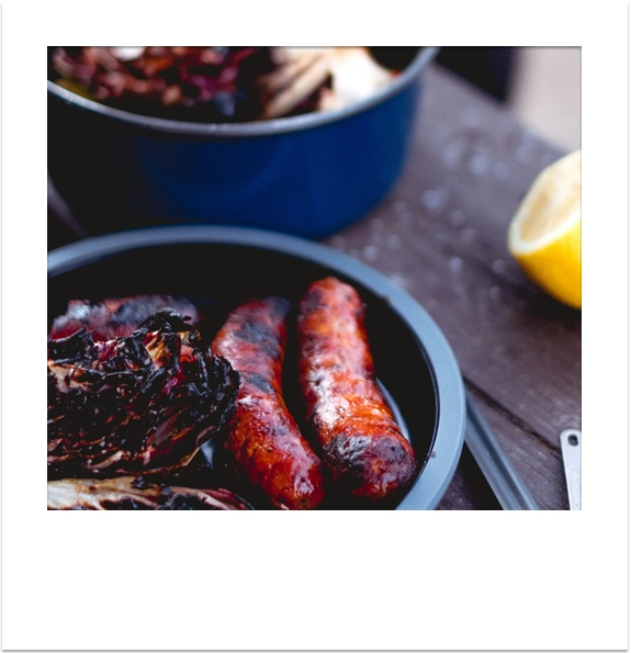 Cooked sausages and vegetables prepared on a camping BBQ.