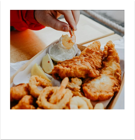 Freshly cooked fish, chips, and calamari in a takeaway box.