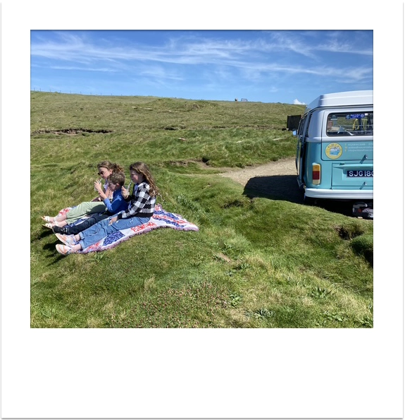 A family enjoying a coastal picnic next to a vintage VW campervan.