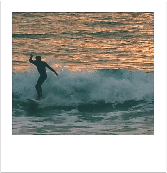 Silhouette of a surfer riding a wave at sunset in Cornwall.