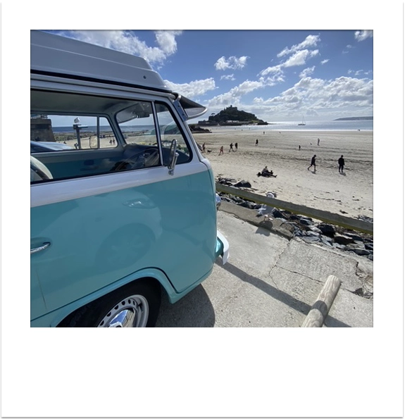 A classic turquoise VW campervan parked on the coast looking across the beach to St Michael's Mount.